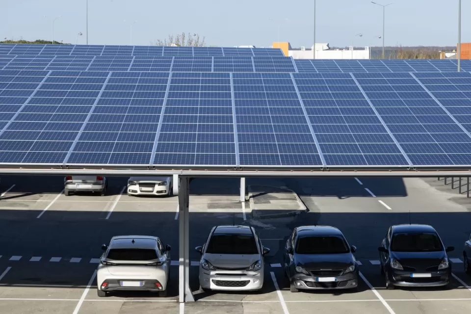Solar panels installed as shade panels over parking lot with small cars parked underneath.